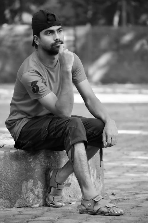 A Grayscale Photo of a Man Sitting on the Street