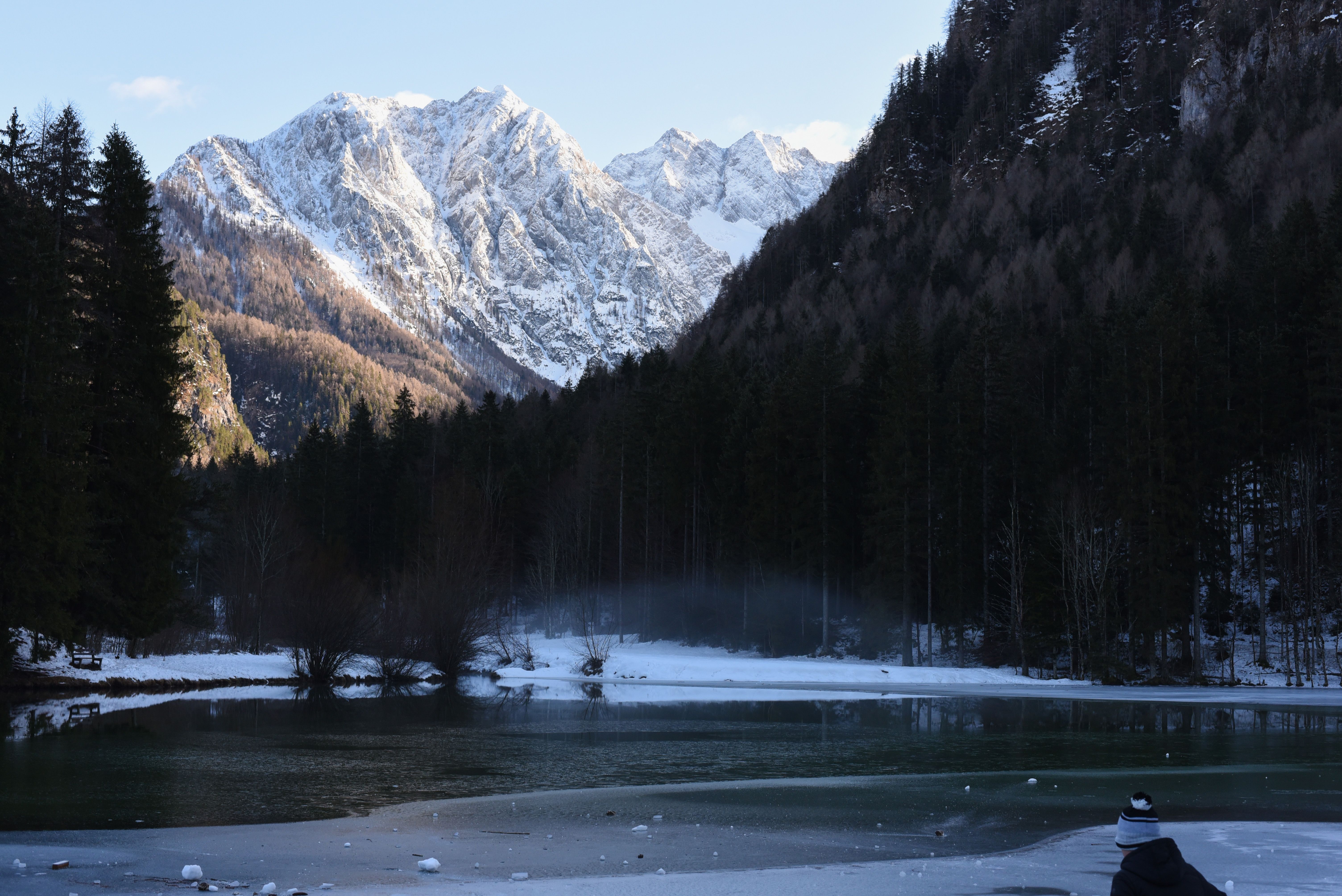 A frozen mountain lake ringed by conifers below snow-covered peaks