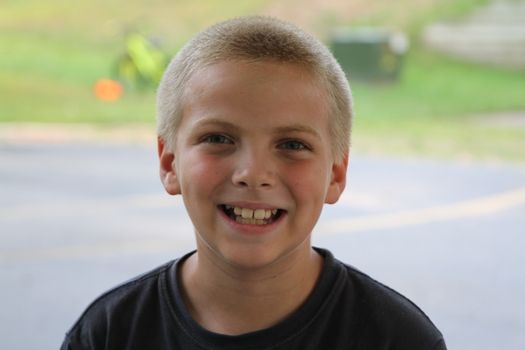 A cheerful young boy with a bright smile in an outdoor summer setting.