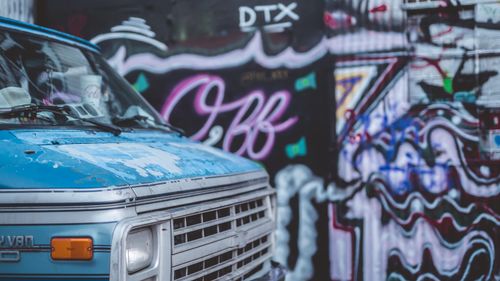 Free A weathered blue van parked beside a vibrant graffiti wall, creating an urban art scene. Stock Photo