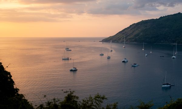 Tranquil view of sailboats and yachts in Phuket, Thailand with a warm sunset horizon.