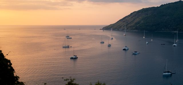 Tranquil view of sailboats and yachts in Phuket, Thailand with a warm sunset horizon.