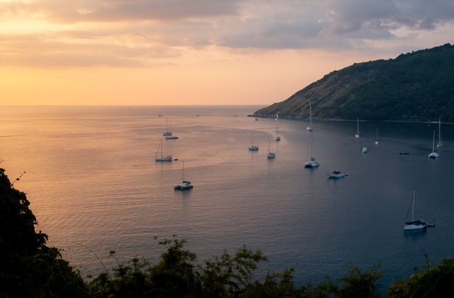 Tranquil view of sailboats and yachts in Phuket, Thailand with a warm sunset horizon. — arriving in Phuket
