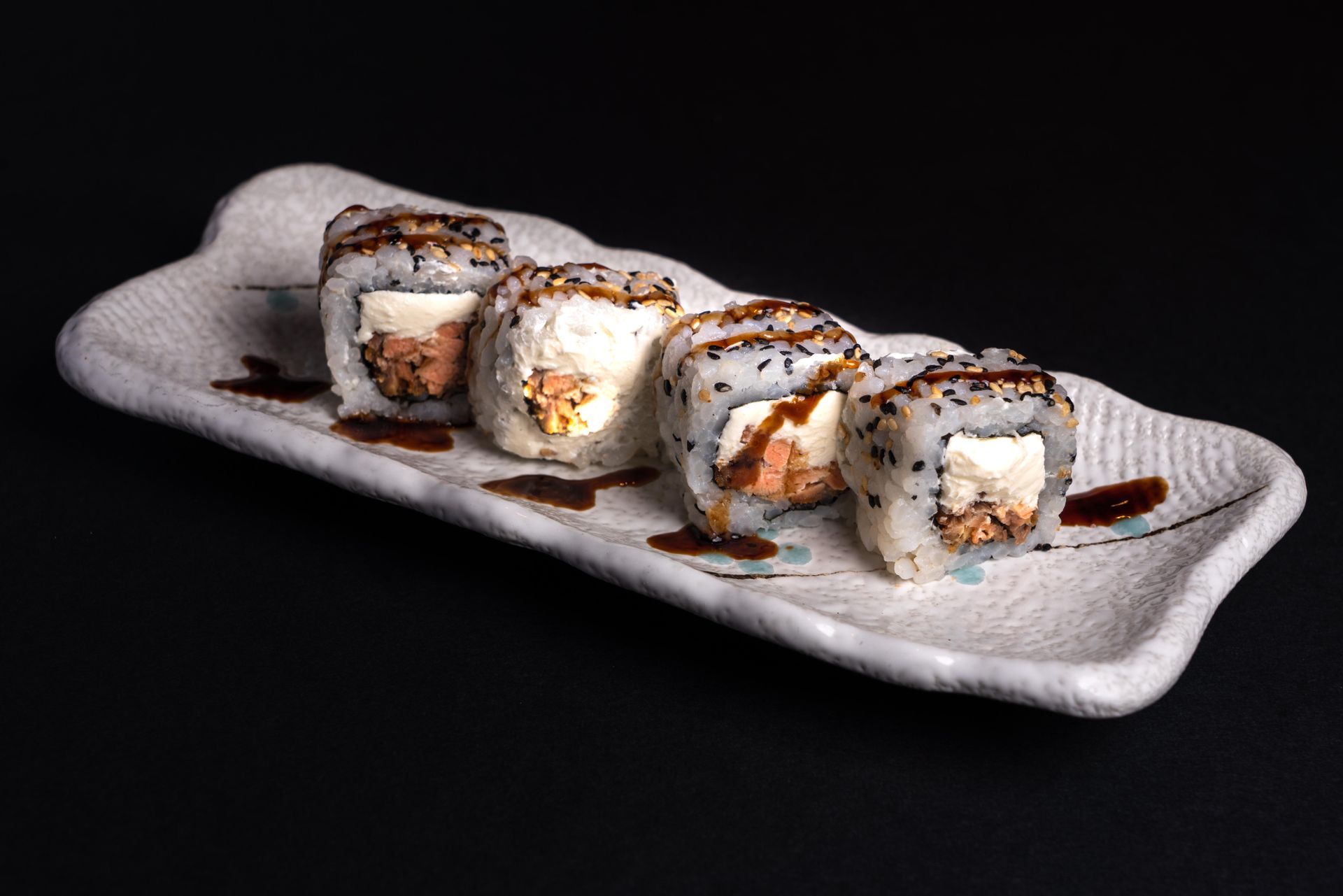 Close-up of sushi rolls with cream cheese and salmon on a ceramic platter.