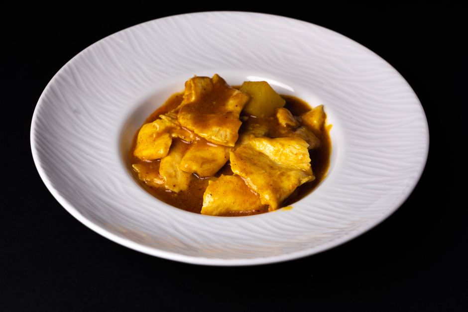 Close-up of a delicious chicken curry dish beautifully plated in a white ceramic bowl on a dark background.