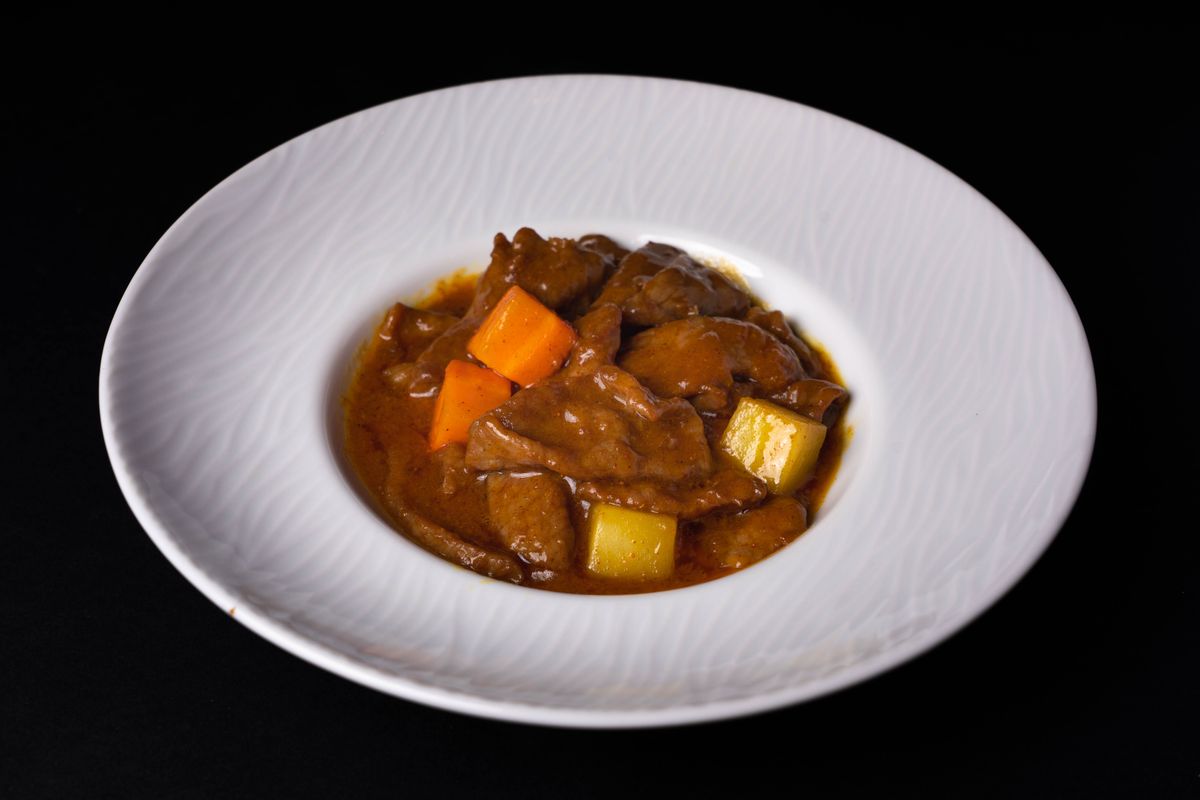 White ceramic bowl of beef stew showing chunks of tender beef, carrot pieces and potato cubes in rich brown gravy