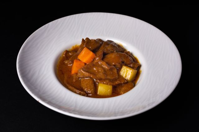 Delicious beef stew with carrots and potatoes served in a white ceramic bowl on a dark background.