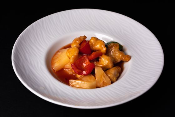 Battered sweet and sour pork with pineapple and red pepper in a wide white bowl