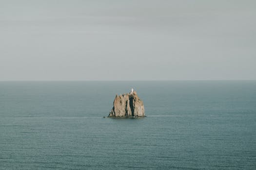 Lone rock with lighthouse in the calm sea, ideal for tranquil seascapes.