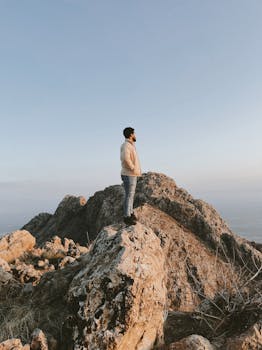 A man stands on a rocky mountain peak under a clear blue sky in Ranya, Iraq.