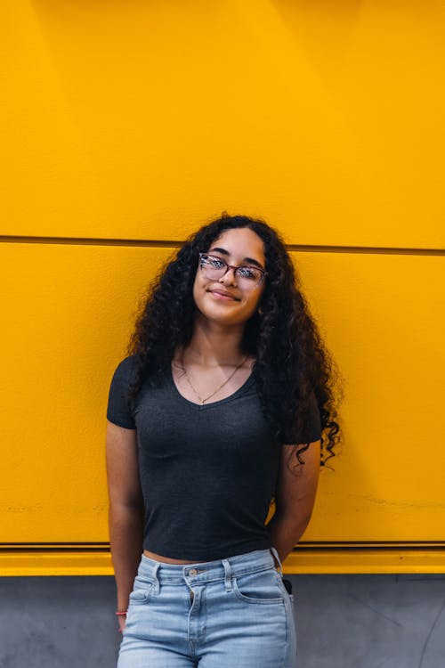 Woman in Black Shirt standing against a Yellow Wall 
