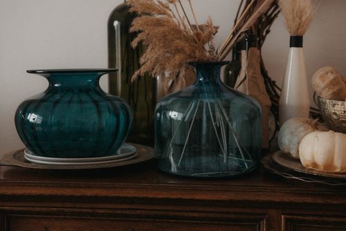 Free Autumn-themed arrangement with glass vases, dried plants, and pumpkins on a wooden dresser. Stock Photo