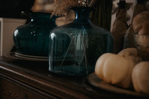 Free Close-up of blue glass vases, dried plants, and white pumpkins on a wooden dresser, creating a rustic decor setting. Stock Photo