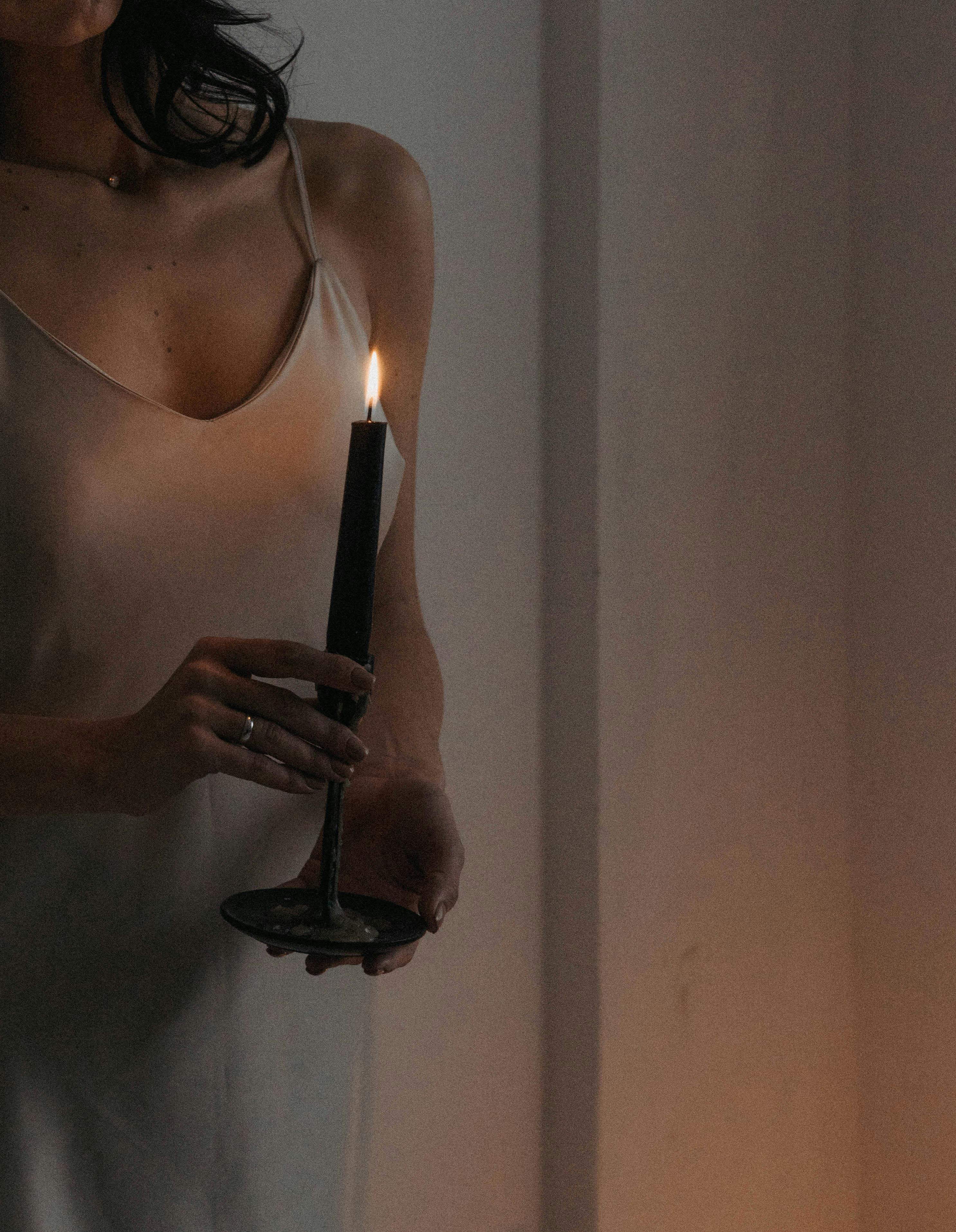 A stylish woman holding a candle, casting a warm glow in a serene setting.