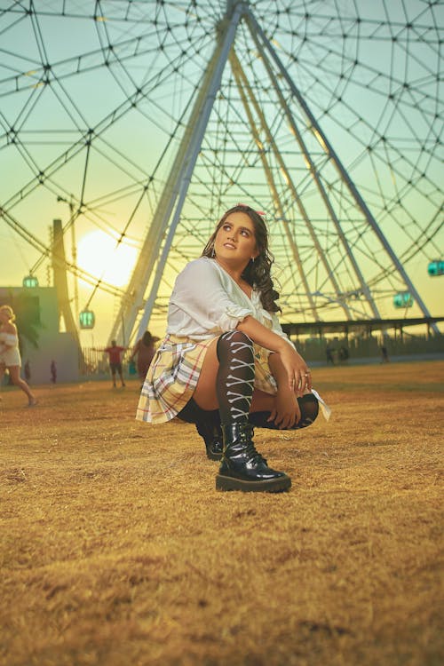 Free Woman in White Long Sleeve Shirt and Black and White Plaid Skirt Sitting on Brown Field Stock Photo