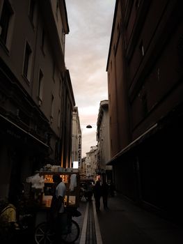 A narrow city alley at dusk with silhouetted buildings and street vendors.