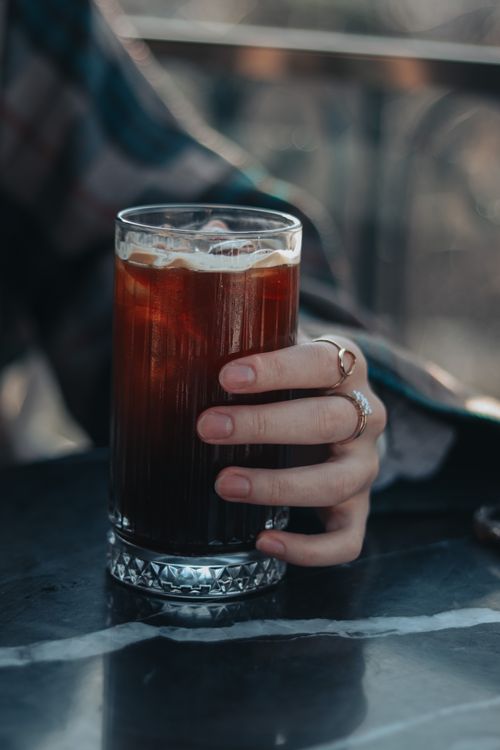 Free A close-up shot of a hand holding a refreshing iced coffee on a table, perfect for beverage themes. Stock Photo