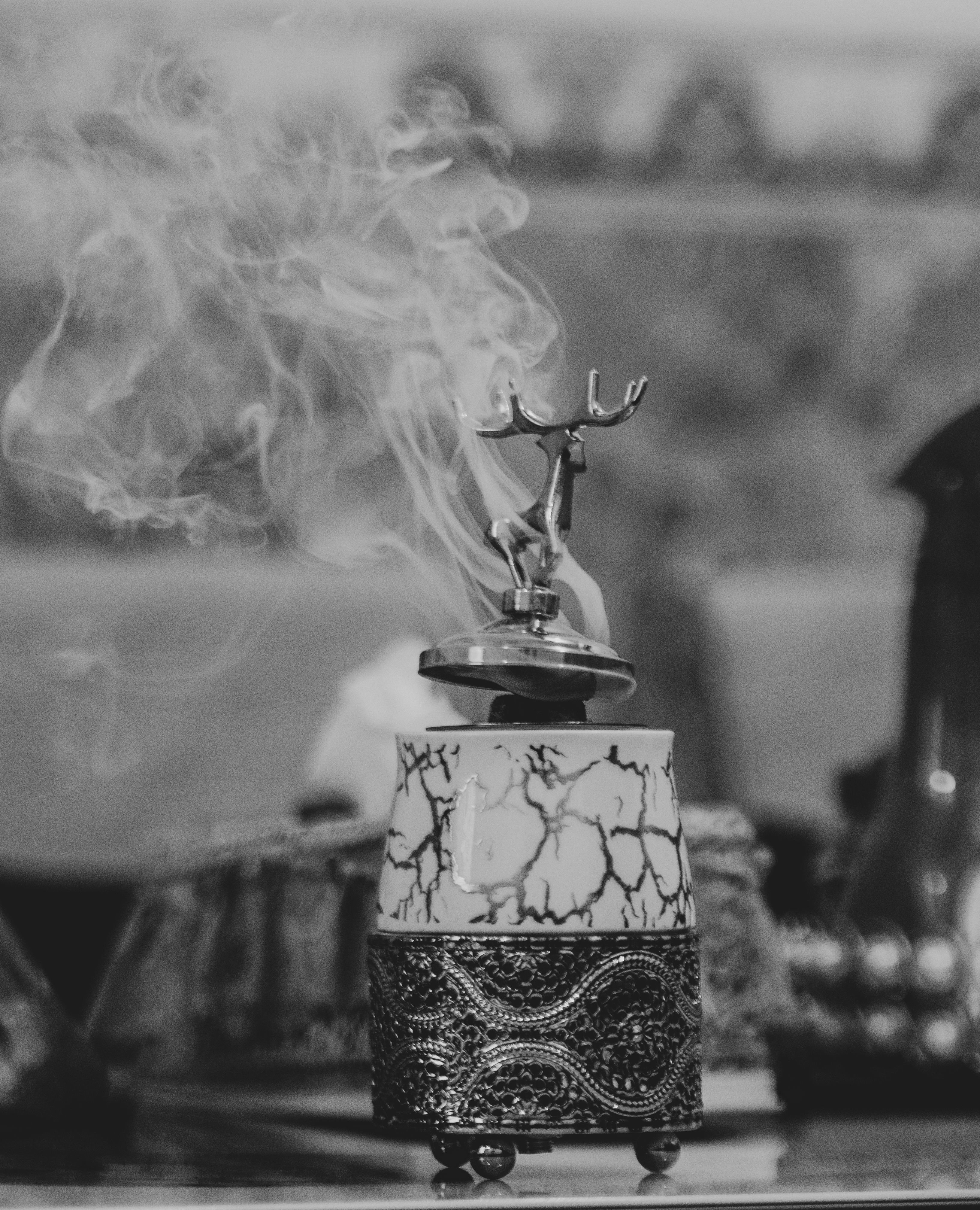 Black and white close-up of an ornate incense holder with smoke swirling upwards.