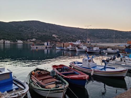 Free A serene view of colorful fishing boats docked in a harbor at sunset with calm waters and a hilly backdrop. Stock Photo