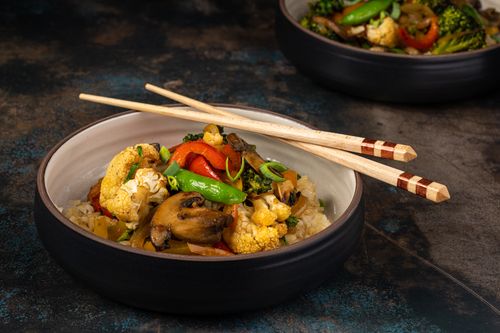 Free A delicious close-up of a colorful vegetable stir fry in a ceramic bowl with chopsticks. Stock Photo