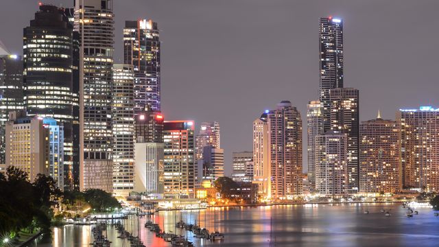 A breathtaking view of Brisbane's illuminated skyline at night with reflections on the river. — lounges at Brisbane Airport