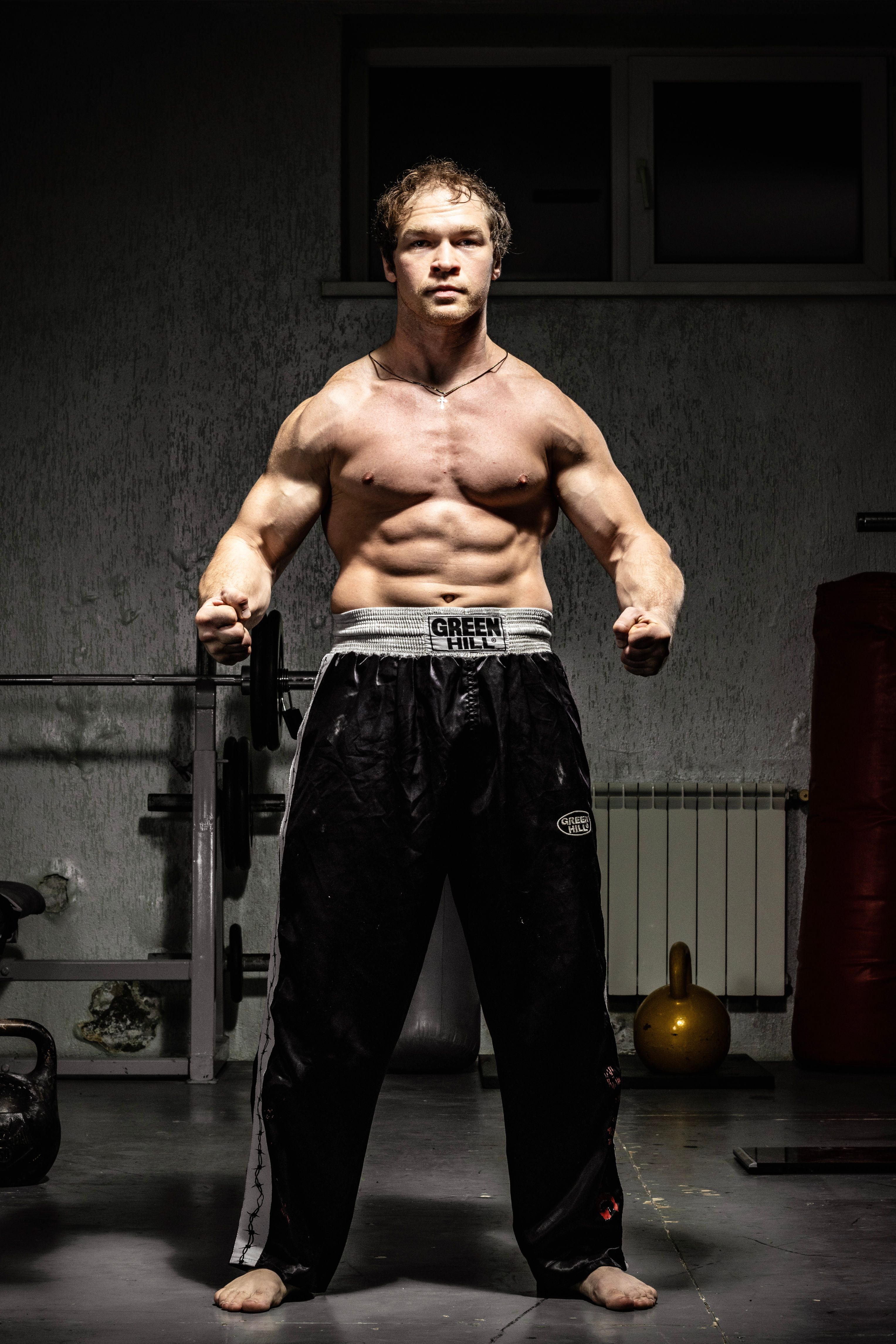 Strong male bodybuilder showcasing muscles in a dimly lit gym environment.