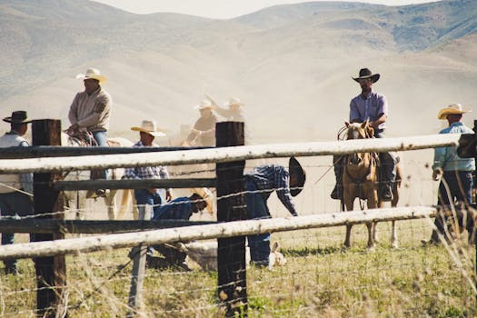 Rural landscape with cowboys on horseback wrangling cattle in a dusty field.