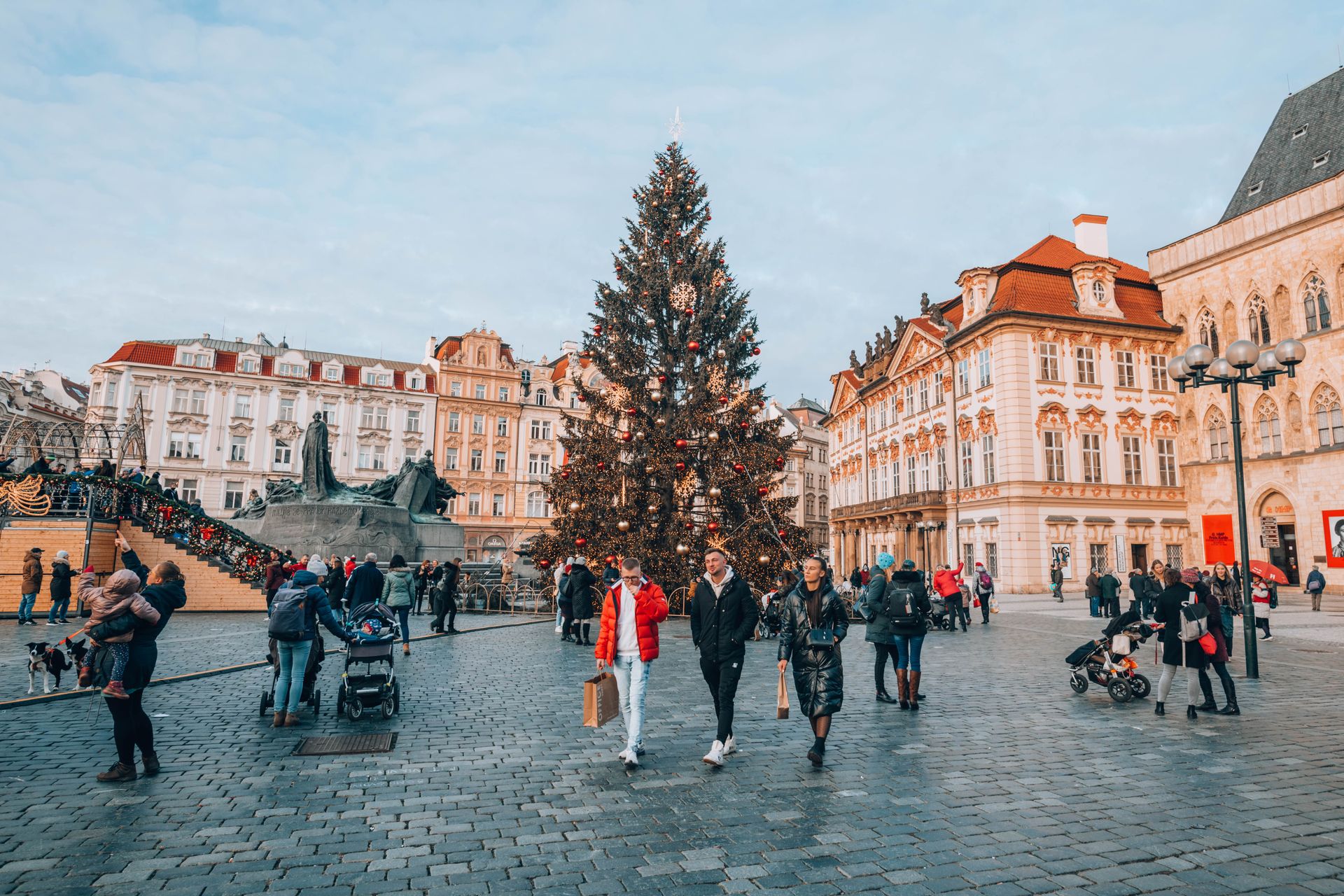 People walking through a festive Christmas market in a historic European town square during winter.