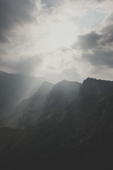Captivating sun rays break through clouds over a rugged mountain landscape, evoking serenity and awe.