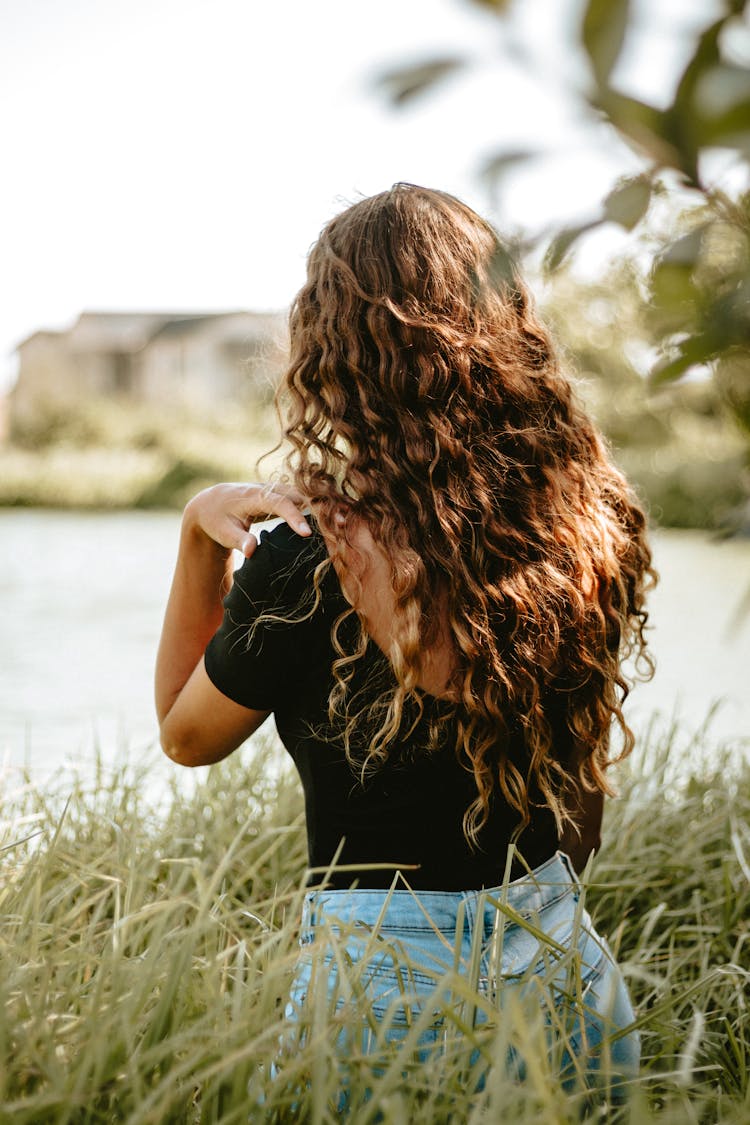 Back And Curly Hair Of Girl Standing In Tall Grass