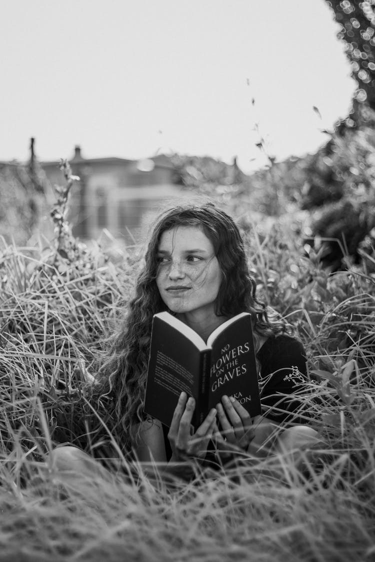 Girl Sitting In Tall Grass Reading Book