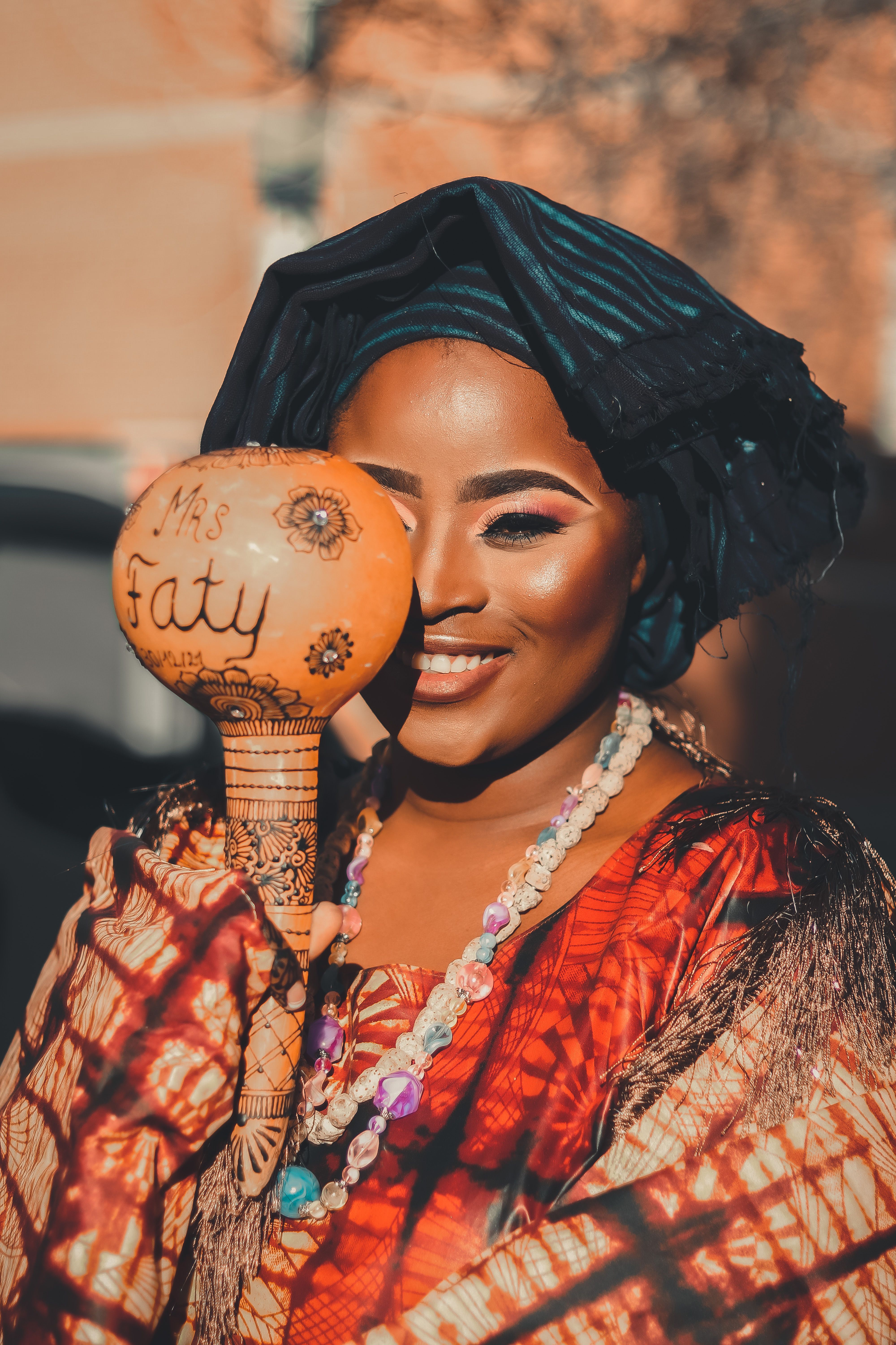 A joyful woman in colorful traditional clothing holding a decorated rattle outdoors.