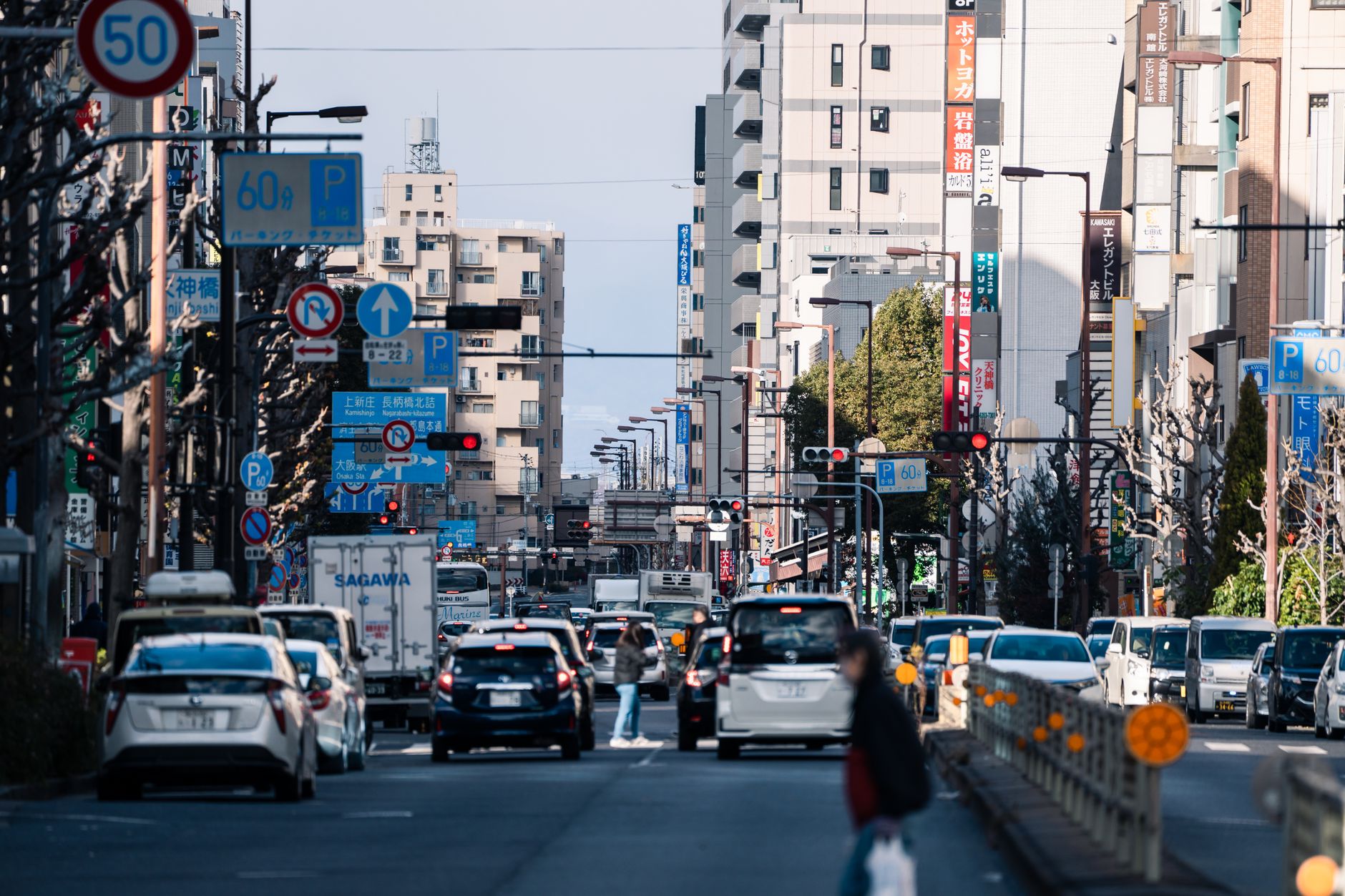 Vibrant urban street in Osaka with bustling traffic and city buildings on a sunny day.