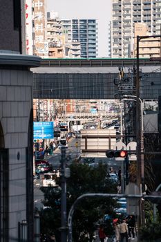 Urban scene in Osaka with bustling streets and railway bridge overhead, showcasing modern Japanese architecture.