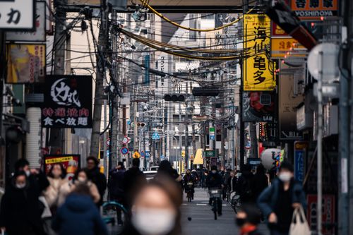 Free Crowded street in Osaka, Japan bustling with masked pedestrians and vibrant advertising signs. Stock Photo