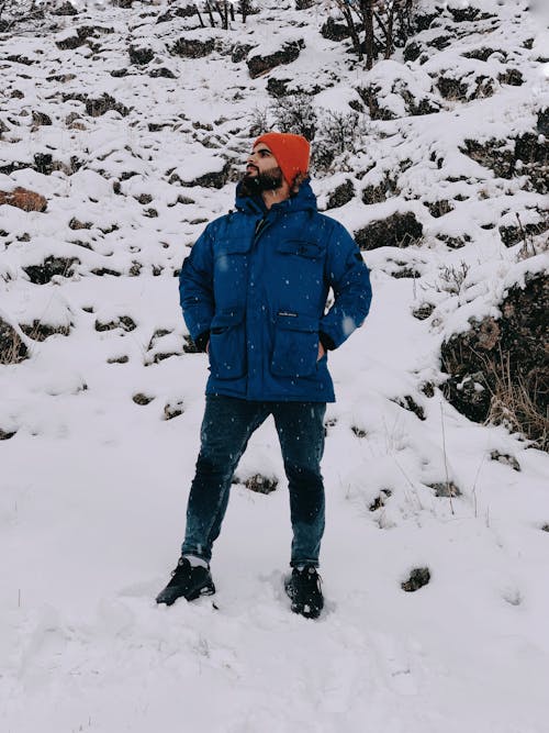 A Man in Blue Jacket Standing on Snow Covered Ground