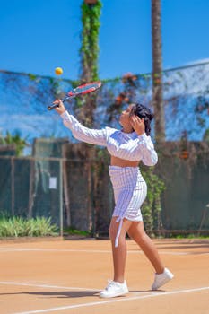 African American woman in stylish attire playing tennis on a sunny outdoor court.