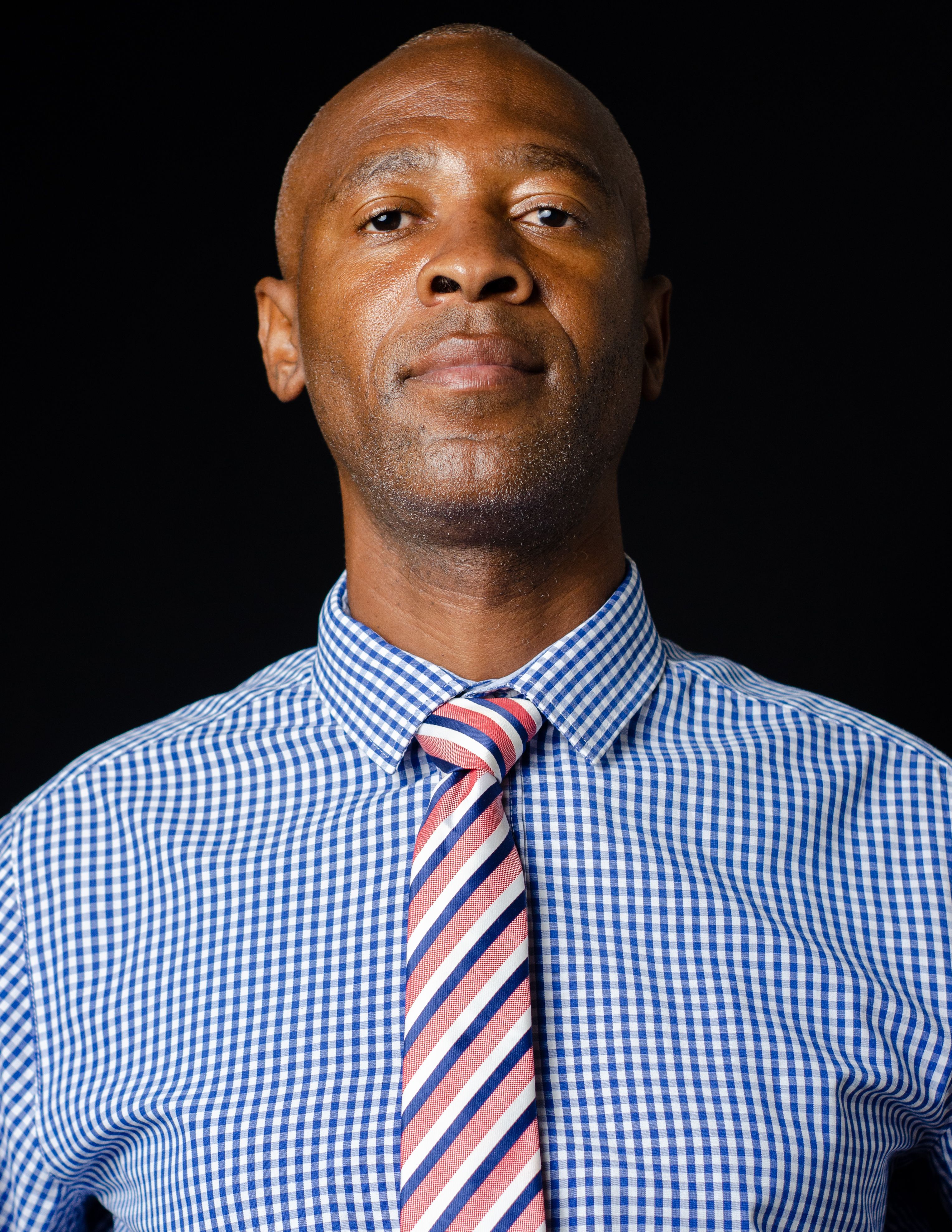 Portrait of an adult African American man in a formal shirt and striped tie, standing confidently.
