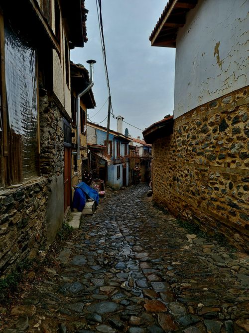 Free Explore a narrow, overcast cobblestone alley in a historic village surrounded by rustic buildings. Stock Photo