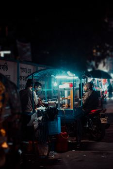 A bustling street food cart at night, illuminated by vibrant blue lights, creating a lively atmosphere.