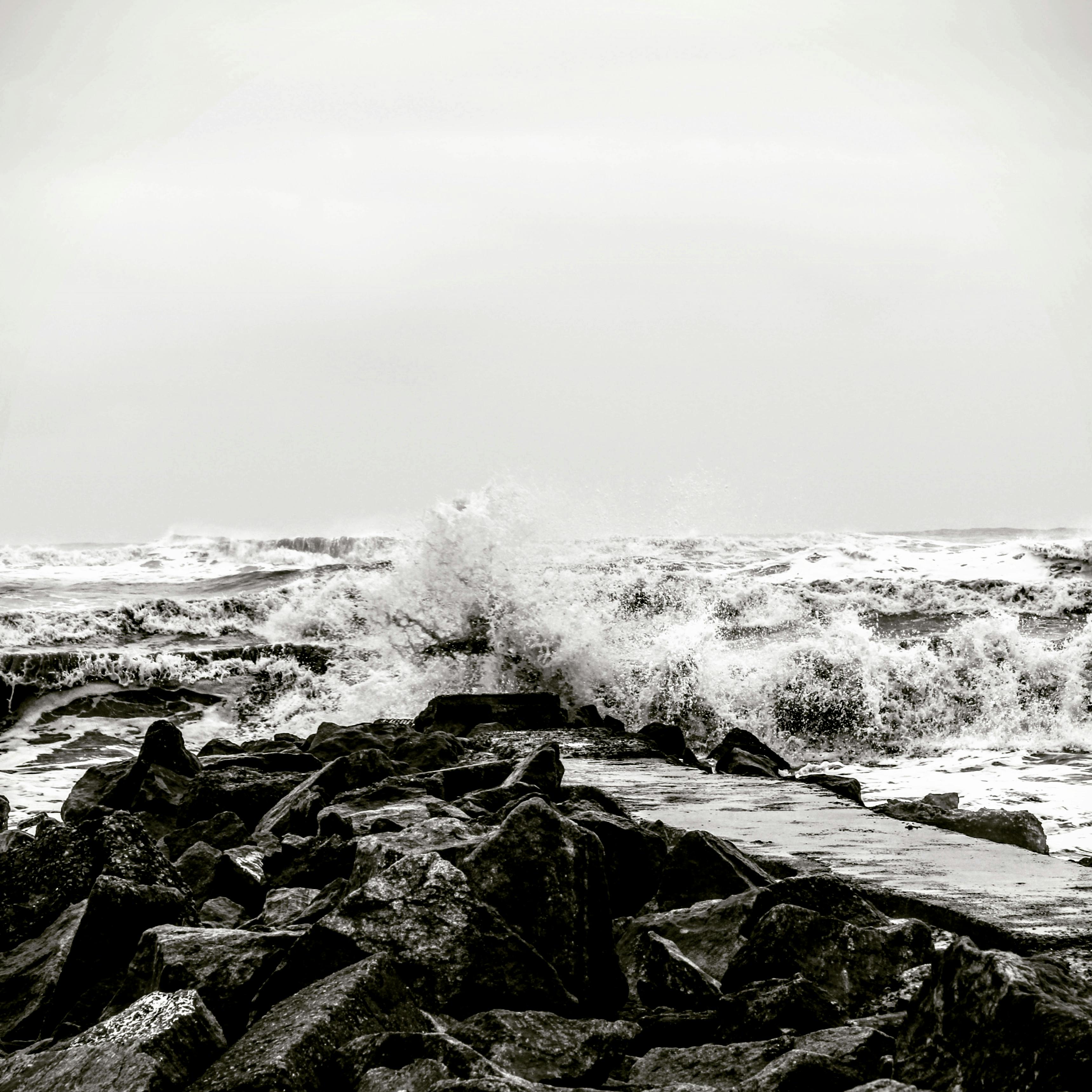 Dramatic black and white photo capturing waves crashing on rocky coastline during a storm.