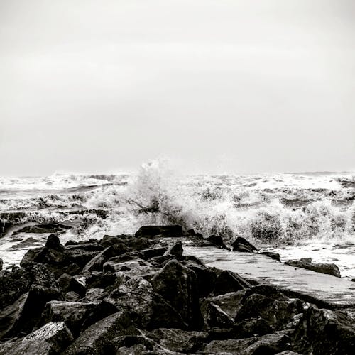 Black and White Photo of Rough Sea and a Rocky Coastline 