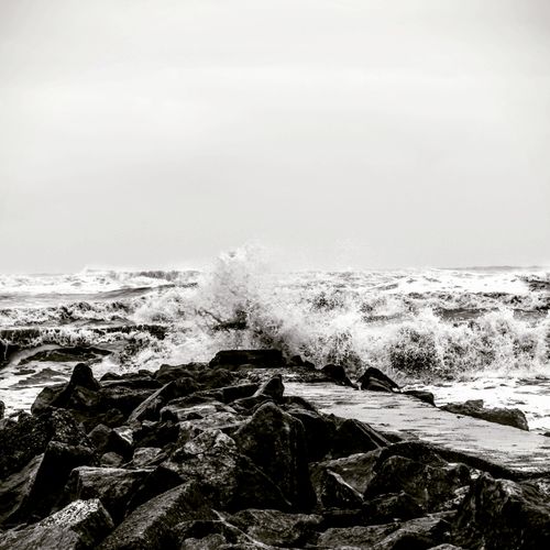 Free Dramatic black and white photo capturing waves crashing on rocky coastline during a storm. Stock Photo
