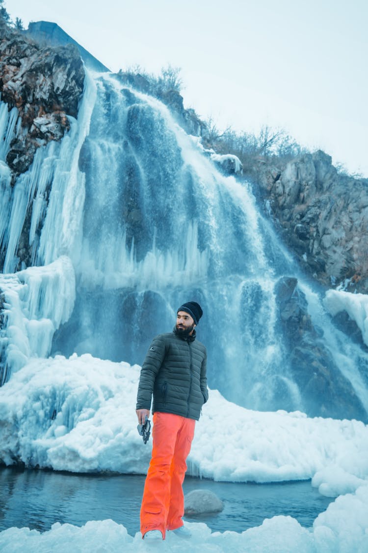 Man Standing Near Frozen Waterfall In Nature