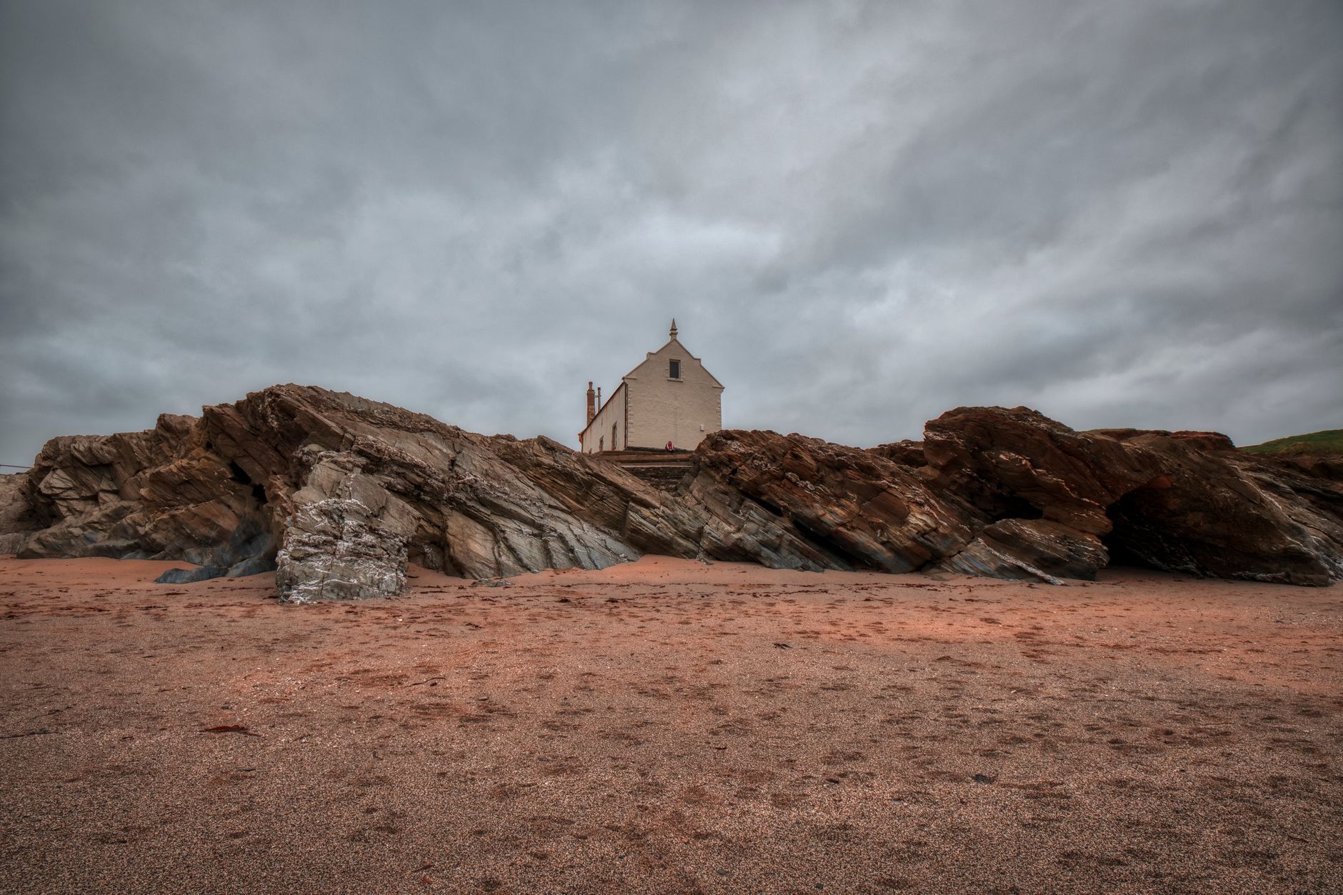 Explore the dramatic cliff and historic chapel at Newquay beach, England's rugged coast.