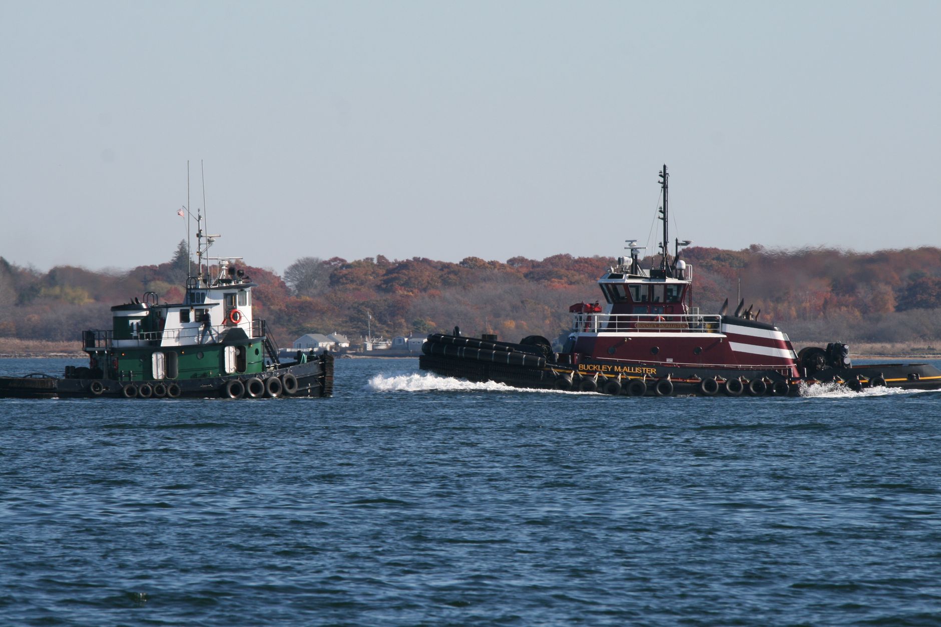 Two tugboats navigate the picturesque waterway of Massachusetts, showcasing maritime transport and autumn scenery.