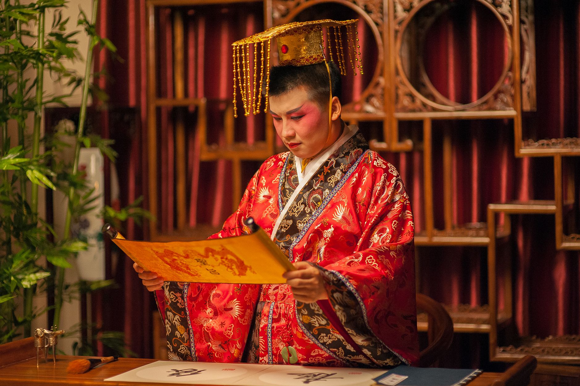 A person in traditional Chinese costume reading a scroll in a decorated room.