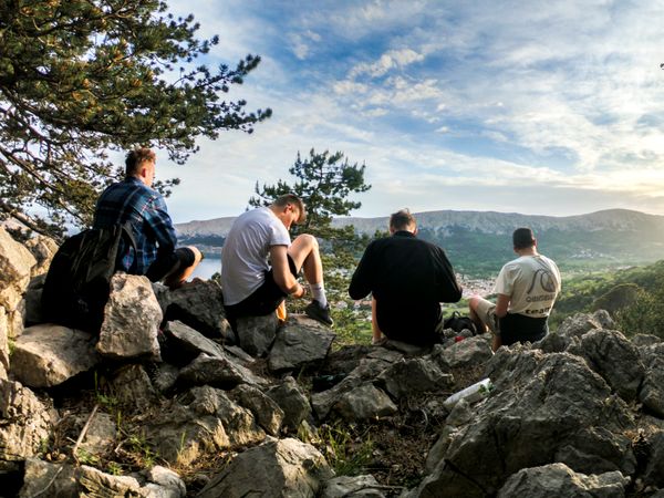 Four men seated together on rocks overlooking a valley at golden hour