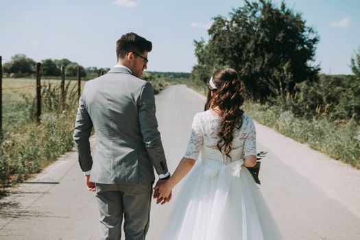 Newlywed couple holding hands and walking down a scenic road in Romania on a sunny day.