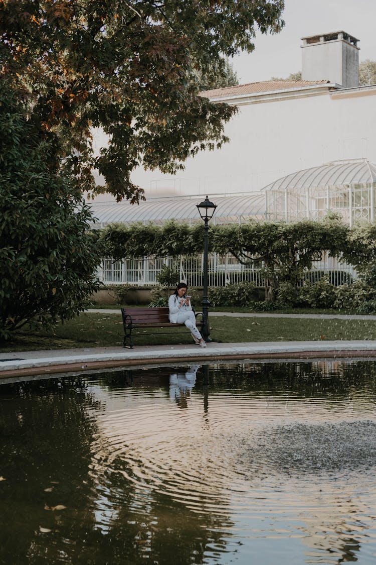 Woman Sitting On A Park Bench By A Pool